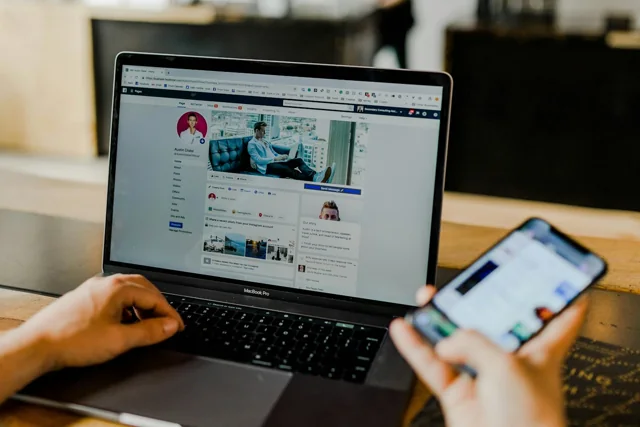 Person using a laptop and smartphone with social media pages